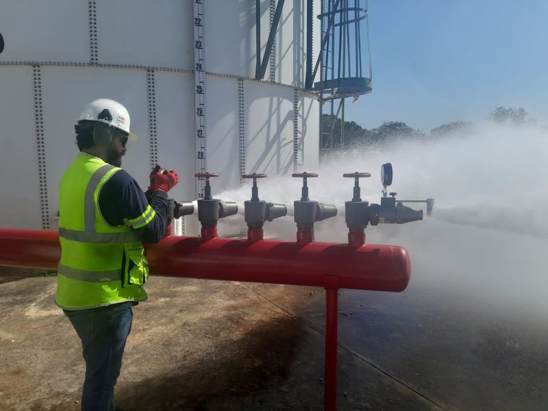 Técnico con casco y chaleco probando un colector rojo de hidrantes con descarga de agua